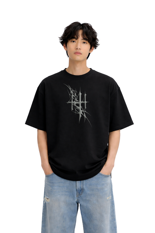 Model wearing oversized black streetwear t-shirt with silver tribal graphic, blue jeans