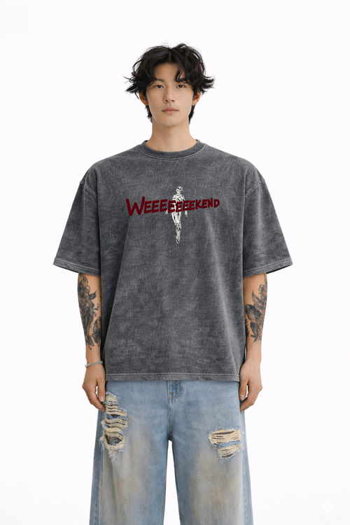 Man wearing oversized washed black t-shirt with 'WEEEEEEKEND' text and skeleton graphic, styled with ripped jeans.